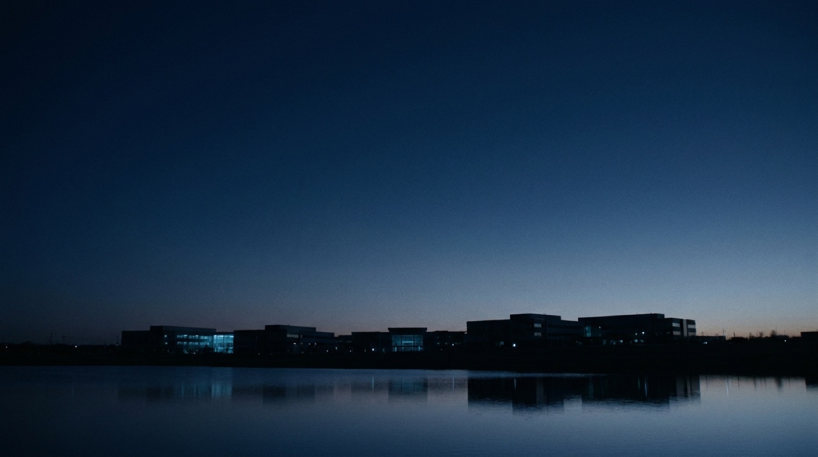 Calm dusk horizon over a technology campus reflected in still water